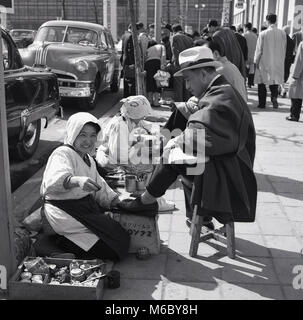 1950er Jahre, Histrocial, Tokio, japanische Geschäftsleute sitzen om Tools auf dem Bürgersteig, eine Schuhputzmaschine/-service von der weiblichen Arbeitnehmer draußen auf der Straße. Stockfoto