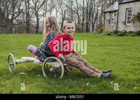 Geschwister sind posieren für die Kamera, während er auf dem Go Kart im Garten. Stockfoto