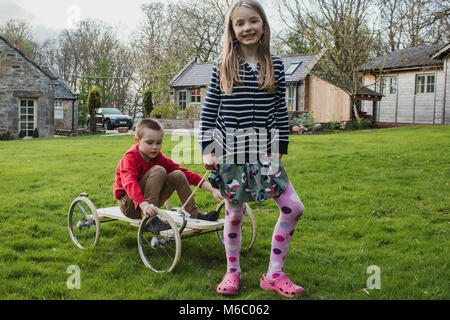 Geschwister sind posieren für die Kamera mit einem Go Kart im Garten. Stockfoto