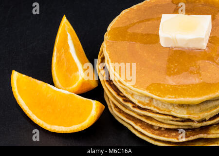 Stapel Pfannkuchen in Sirup mit Orangen auf dunklem Hintergrund. Stockfoto