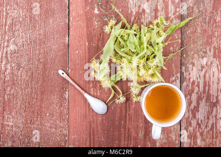 Linden Kaffee in einer Tasse auf einem hölzernen Hintergrund. Verstreut duftenden Linden Blumen. Ansicht von oben Stockfoto