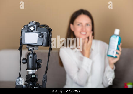 Lächelnde Junge weibliche Blogger halten Produkt Aufnehmen von Videos mit der Kamera zu Hause. Stockfoto