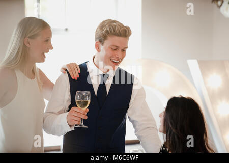 Junge Paare sind Geselligkeit mit anderen Gästen an einem Hochzeit sie an der Veranstaltung teilnehmen. Sie trinken Champagner und Gespräch mit einer älteren Frau, die sitti ist Stockfoto