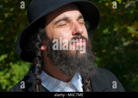 Außenbereich sonnige helle Porträt einer jungen orthodoxen jüdischen Mann mit Augen mit schwarzen Bart, Hut und Kostüm geschlossen Stockfoto