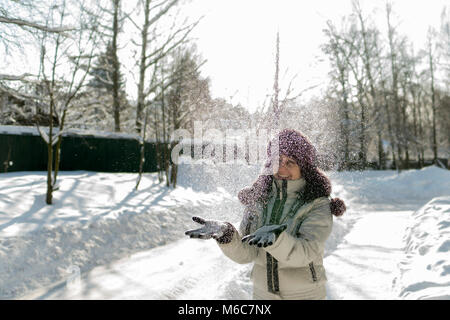 Hält eine Frau eine Handvoll Schnee in den Händen und bläst. Winter im Wald. Die sonne funkelt. Tag, Russland. Stockfoto