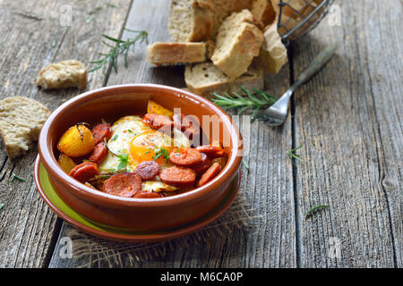 Spanische Tapa: Würzig Chorizo Wurst mit Spiegelei und Kartoffeln in einem Terra Cotta cazuela Gericht serviert. Stockfoto