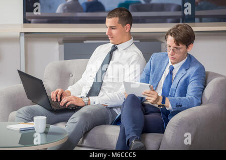 Zwei junge Unternehmer in Office Lobby sitzen und mit Laptop und digitale tablet device Stockfoto