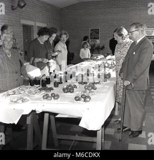 1960, historische, Besucher einer Kirche fundraising Fete die hausgemachten Marmeladen, Kuchen und Obst auf dem Display im Inneren, England, BRITISCHE Studie. Stockfoto