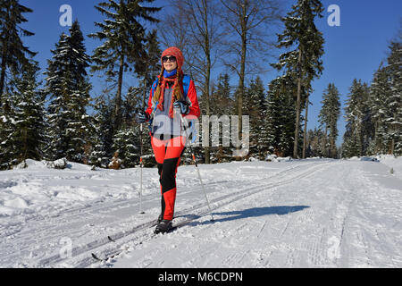 Frau in der Farbe Kleid auf Langlaufskiern unter Bäumen, beschichtet mit dem Schnee in den Bergen in Polen Stockfoto