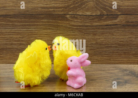 Zwei gelbe Hühner und ein rosa Häschen auf einem alten Holz- Zähler. Eine interessante Ostern Dekoration. horizontale Ansicht. Stockfoto