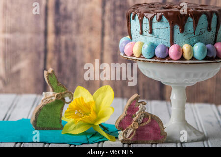 Blaue Milchglas-Torte mit Schokolade tropfen Zuckerguss und Ostereier in einer rustikalen Umgebung Stockfoto