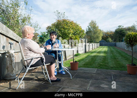 Ein Student Unterkunft host sitzt mit ihrem International Student im Garten Tee zu trinken und zu reden. Stockfoto