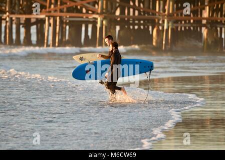 Zwei männliche Surfer, die surfbretter bei Sonnenuntergang, Wandern am Strand mit Pacific Beach Crystal Pier im Hintergrund in San Diego, Kalifornien, USA Stockfoto