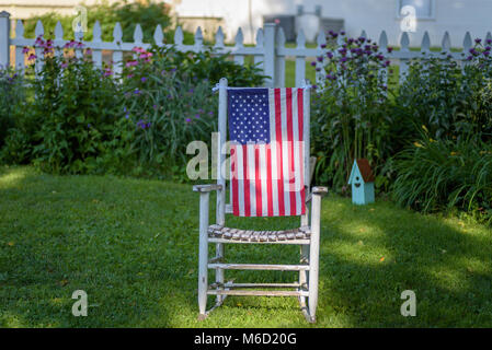 Nahaufnahme eines leeren urigen alten Schaukelstuhl mit amerikanischer Flagge hängt über der Rückseite im Garten Stockfoto