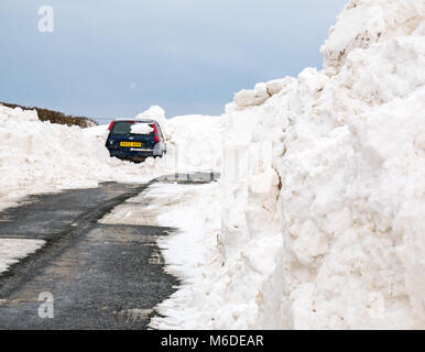 East Lothian, Schottland, Vereinigtes Königreich, 3. März 2018. UK Wetter: Lokale Straßen beginnen, gelöscht werden, aber die Bewohner sind immer noch klemmt, es sei denn, Sie haben ein 4x4. Die lokale B Straße geschlossen ist von einem riesigen Schnee Bank und ein Auto ist in einem snowbank begraben Stockfoto