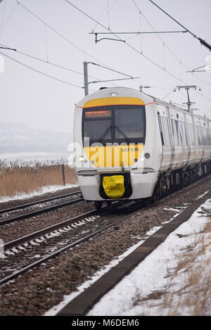 Der C2C-Eisenbahnzug führt durch den schneebedeckten Hadleigh Country Park und die Felder der Hadleigh Marshes an nebelhaltigen Wintertagen während des Ostwetterphänomens. Essex ländlich Stockfoto