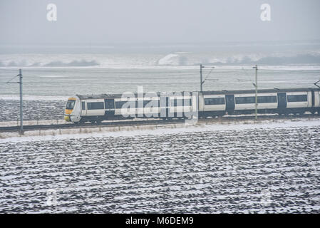 Der C2C-Eisenbahnzug führt durch den schneebedeckten Hadleigh Country Park und die Felder der Hadleigh Marshes an nebelhaltigen Wintertagen während des Ostwetterphänomens. Essex ländlich Stockfoto