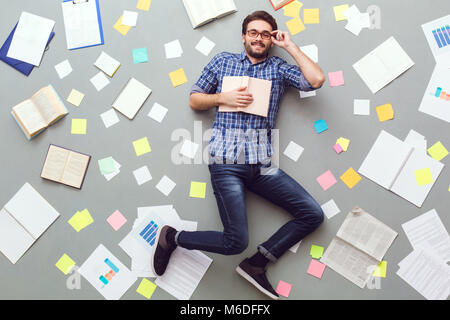 Junger Mann auf grauem Hintergrund mit Papieren und Hinweise Buch isoliert Stockfoto