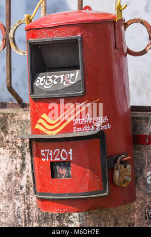 Madikeri, Indien - 31. Oktober 2013: Nahaufnahme von roten öffentlichen Briefkasten am Zaun und schmutzige Wand. Stockfoto