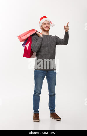 Weihnachten Konzept - attraktiven jungen kaukasischen Mann überraschend schockierende Holding Einkaufstasche und Zeigefinger vor. Stockfoto