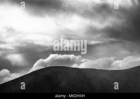 Eine schwarze und weiße zeitlose Erfassung von einer Person zu Fuß auf den Krater des massiven Mount Bromo Vulkan unter dem schweren Wolken Stockfoto