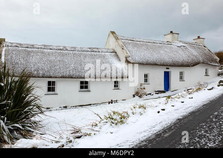 Schnee bedeckt strohgedeckten Irish cottage in country lane auf Valentia Island, County Kerry, Irland Stockfoto