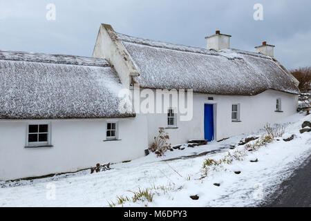 Schnee bedeckt strohgedeckten Irish cottage in country lane auf Valentia Island, County Kerry, Irland Stockfoto