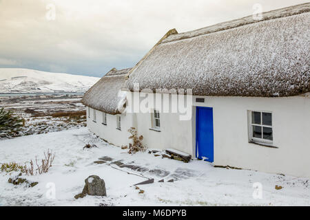 Schnee bedeckt strohgedeckten Irish cottage in country lane auf Valentia Island, County Kerry, Irland Stockfoto