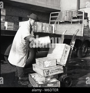 1950er Jahre, historisches Bild eines älteren Pförtners, der Holzkisten aus Kabeljaufilet von einem Lastwagen auf einen Sackkarren- oder Portierwagen vor dem Billingsgate Wholesale Fish Market, London, England, Großbritannien entlädt. Billingsgate, an der Lower Thames Street in der Stadt London, war zu einem Zeitpunkt der größte Fischmarkt der Welt. Stockfoto