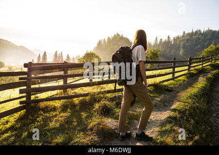 Mädchen mit Rucksack bei einem Spaziergang den Hügel hinauf und genießen die schöne Landschaft bei Sonnenaufgang Stockfoto