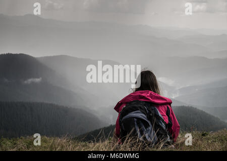 Junge weibliche Wanderer mit Rucksack sitzt im Gras auf dem Hügel in den ukrainischen Karpaten Stockfoto