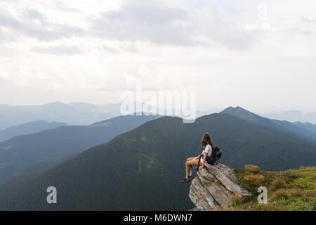 Frau mit touristischen rusksack nimmt Rest oben auf dem Hügel nach dem Erreichen des Ziels in den Karpaten und genießt die schöne Landschaft Stockfoto