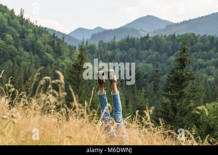 Eine müde Person macht Handstand Rest für Beine in Trekking Schuhe auf einer wunderschönen Wiese in Karpaten zu erhalten Stockfoto