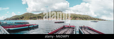 Panorama-aufnahme der Leere Lastkähne auf Kundschaft warten auf der Straße von Tiquina über den Titicaca-see in Bolivien, mit der Stadt San Pedro de Tiquina Stockfoto