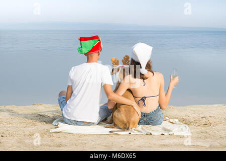 Mann, Frau und Hund in neue lustige Jahr Hüte verbringen viel Zeit am Meer Stockfoto
