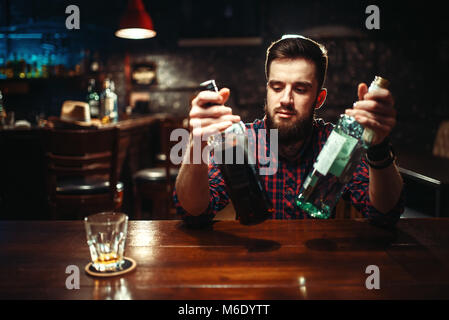 Alkoholische Sitzen an der Theke mit zwei Flaschen Alkohol trinken in Händen. Männliche Person im Pub, Alkoholismus, Trunkenheit Stockfoto