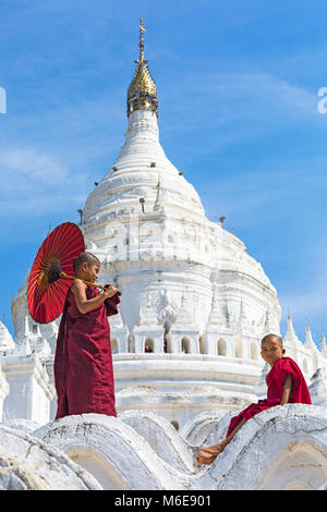 Junge Novizin buddhistische Mönche, einer Holding- und einem Sonnenschirm sitzen an Myatheindan Pagode (auch als Hsinbyume Pagode bekannt), Mingun, Myanmar (Birma) Asien Stockfoto