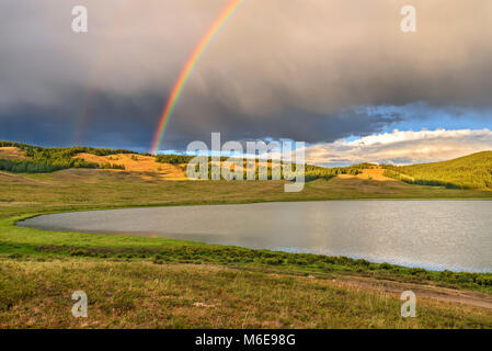 Hellen bunten Regenbogen über die Berge, den See und den Wald nach dem Regen gegen den blauen Himmel mit Wolken im Sommer Stockfoto