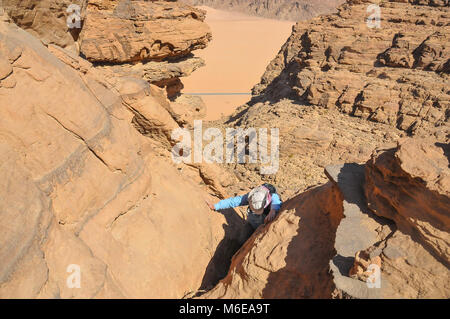 Ein Wanderer klettern in Wadi Rum auf einem Berg mit der Wüste und die asphaltierte Straße in der Senke Stockfoto