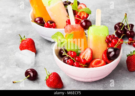 Mehrfarbige Eis am Stiel mit Erdbeere, rote Johannisbeere und Kirsche auf grauem Hintergrund Stockfoto