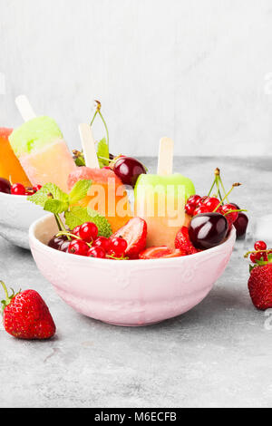 Mehrfarbige Eis am Stiel mit Erdbeere, rote Johannisbeere und Kirsche auf grauem Hintergrund Stockfoto