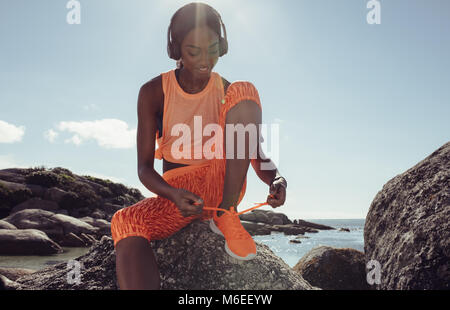 Fit und sportlich junge Frau band ihre Schnürsenkel vor einem Lauf. Läuferin ihre Schnürsenkel binden während der Ausbildung an der felsigen Strand. Stockfoto