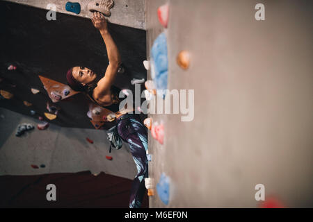 Athletische Frau Bouldern in einer Kletterhalle. Frau Bergsteiger versuchen, für die Griffe beim Klettern in einer Kletterhalle zu erreichen. Stockfoto