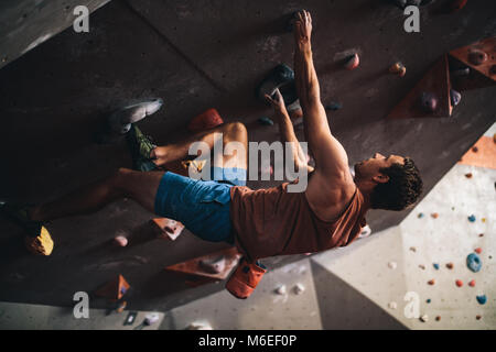 Athletischer mann Bouldern in einer Kletterhalle. Professioneller Kletterer an der Wand den Kopf Klettern in der Kletterhalle. Stockfoto