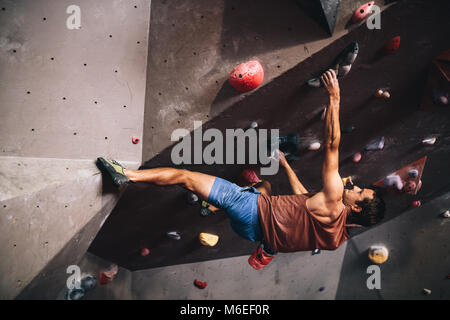 Athletischer mann Bouldern in einer Kletterhalle. Professioneller Kletterer an der Wand den Kopf Klettern in der Kletterhalle. Stockfoto