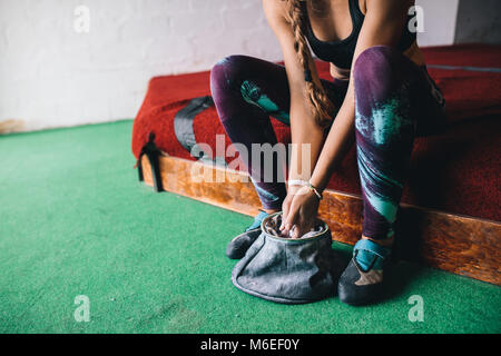 7/8 Schuß von Frau an einem wall Kletterhalle Anwendung magnesium Chalk Pulver auf die Hände aus der Tasche. Stockfoto