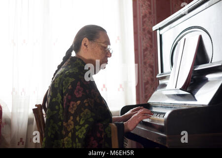 Die alte Dame spielen klassische Musik auf der Seltenheit Klavier zu Hause Stockfoto