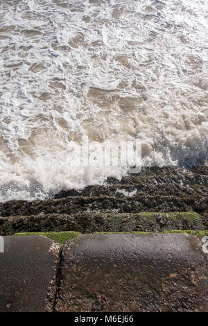 Die Flut an der Waterfront Pfad in der Nähe von Cranbrook mit dem Meer Läppen auf der Promenade Schritte zum Sandstrand. Stockfoto