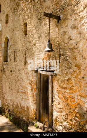 Alte Holztür mit einer kleinen Glocke über es, in stein Wand. Stockfoto