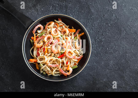 Pfannengerichte mit Udon-nudeln, Shrimps (Garnelen) und Gemüse. Asiatische gesundes Essen, Mahlzeit, Braten im Wok rühren über schwarzen Hintergrund, kopieren. Stockfoto